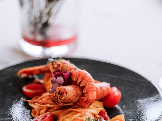 Familienhotel in Sterzing: hoi und herzlich willkommen! Pastagericht mit Garnelen und Kirschtomaten auf einem schwarzen Teller