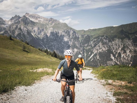 Pflerschtal: accommodation for biking holidays Two cyclists on mountain trail with rocky peaks in background