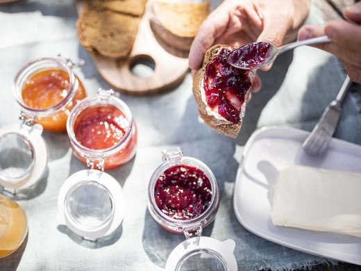 Genuss aus Pflersch: Hotel Panorama Person bestreicht Brot mit roter Marmelade neben Butter und weiteren Marmeladengläsern
