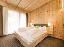 Familienhotel in Sterzing: hoi und herzlich willkommen! Gemütliches Schlafzimmer mit Holzwänden und einem Doppelbett bei Tageslicht