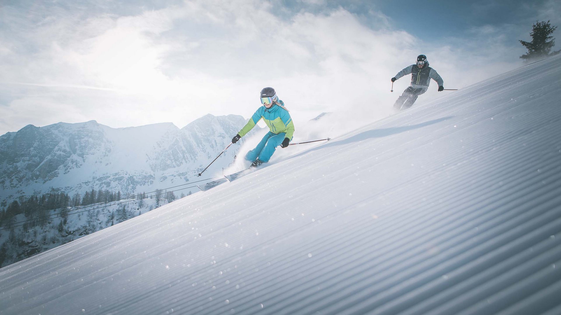Hotel in Ladurns – perfekt für den Winterurlaub! Zwei Skifahrer fahren schnell einen verschneiten Hang mit Bergen im Hintergrund hinab