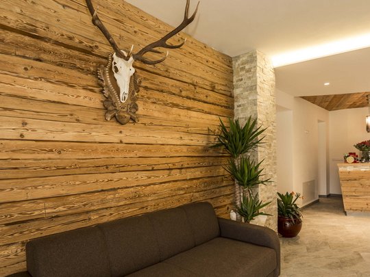 Familienhotel in Sterzing: hoi und herzlich willkommen! Wohnzimmer mit braunem Sofa, Holzwand und Hirschgeweih-Dekoration