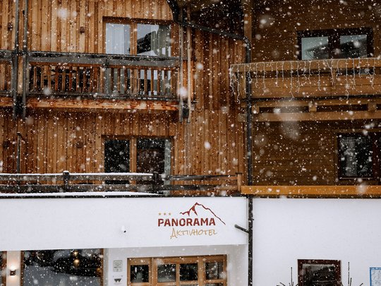 Familienhotel in Sterzing: hoi und herzlich willkommen! Schneefall vor Holzhaus mit Panorama Aktivhotel Eingangsbereich