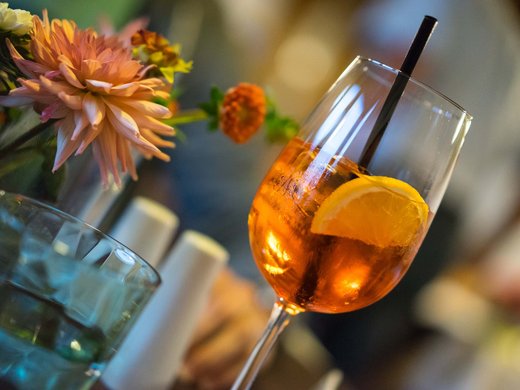 Genuss aus Pflersch: Hotel Panorama Cocktailglas mit Orangenscheibe und Strauß bunter Blumen im Hintergrund