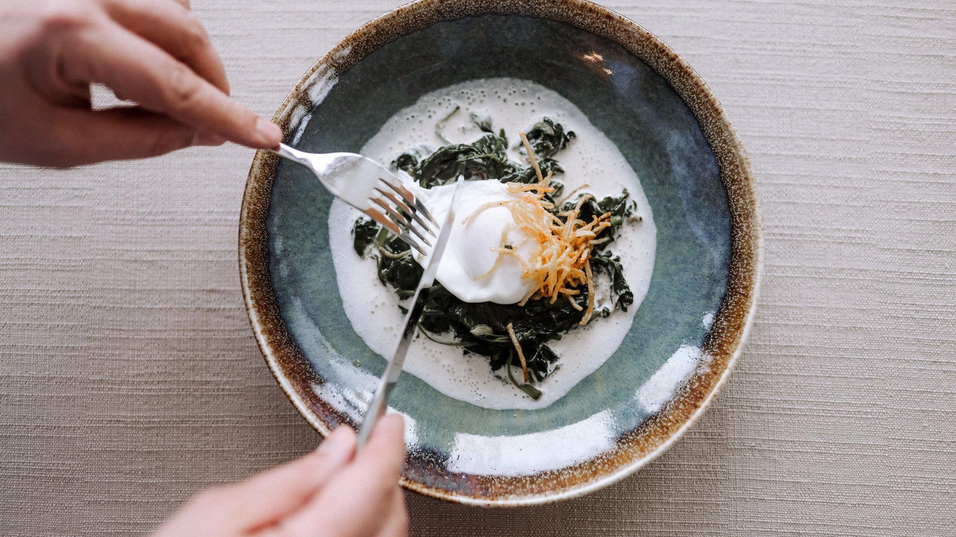 Familienhotel in Sterzing: hoi und herzlich willkommen! Person schneidet pochiertes Ei auf cremigem Spinatgericht in Teller