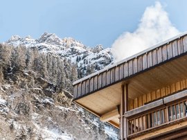 Familienhotel in Sterzing: hoi und herzlich willkommen! Holzhaus mit Rauch und verschneiten Bergen im Hintergrund