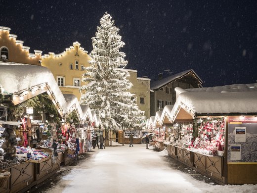 Hotel in Ladurns – perfekt für den Winterurlaub! Weihnachtsmarkt im Winter mit geschmücktem Baum und schneebedeckten Ständen bei Nacht
