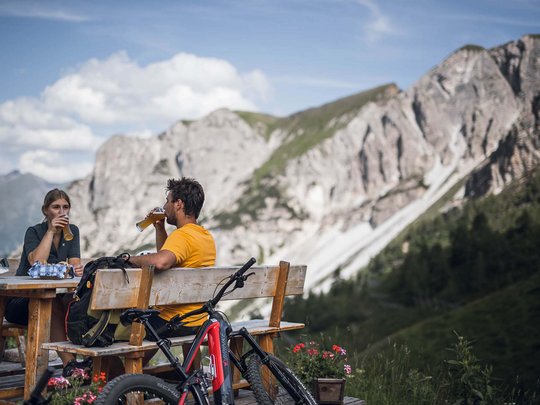 Pflerschtal: accommodation for biking holidays Two cyclists drinking beer on a bench with mountain scenery