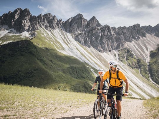 Pflerschtal: accommodation for biking holidays Two mountain bikers riding on a trail below rugged mountain peaks